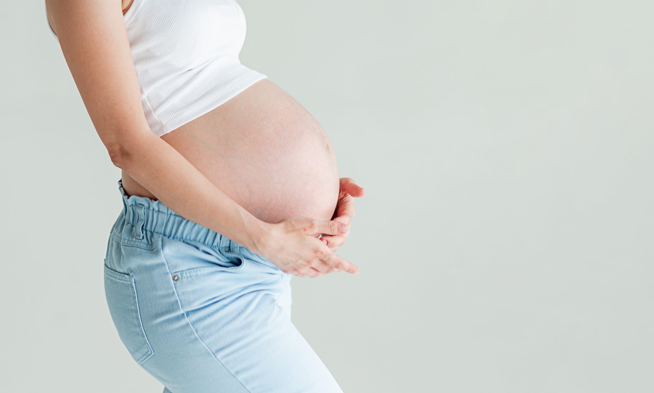 Frau legt beide Hände auf ihren schwangeren Bauch, kurz vor Ende der Schwangerschaft (42. SSW)